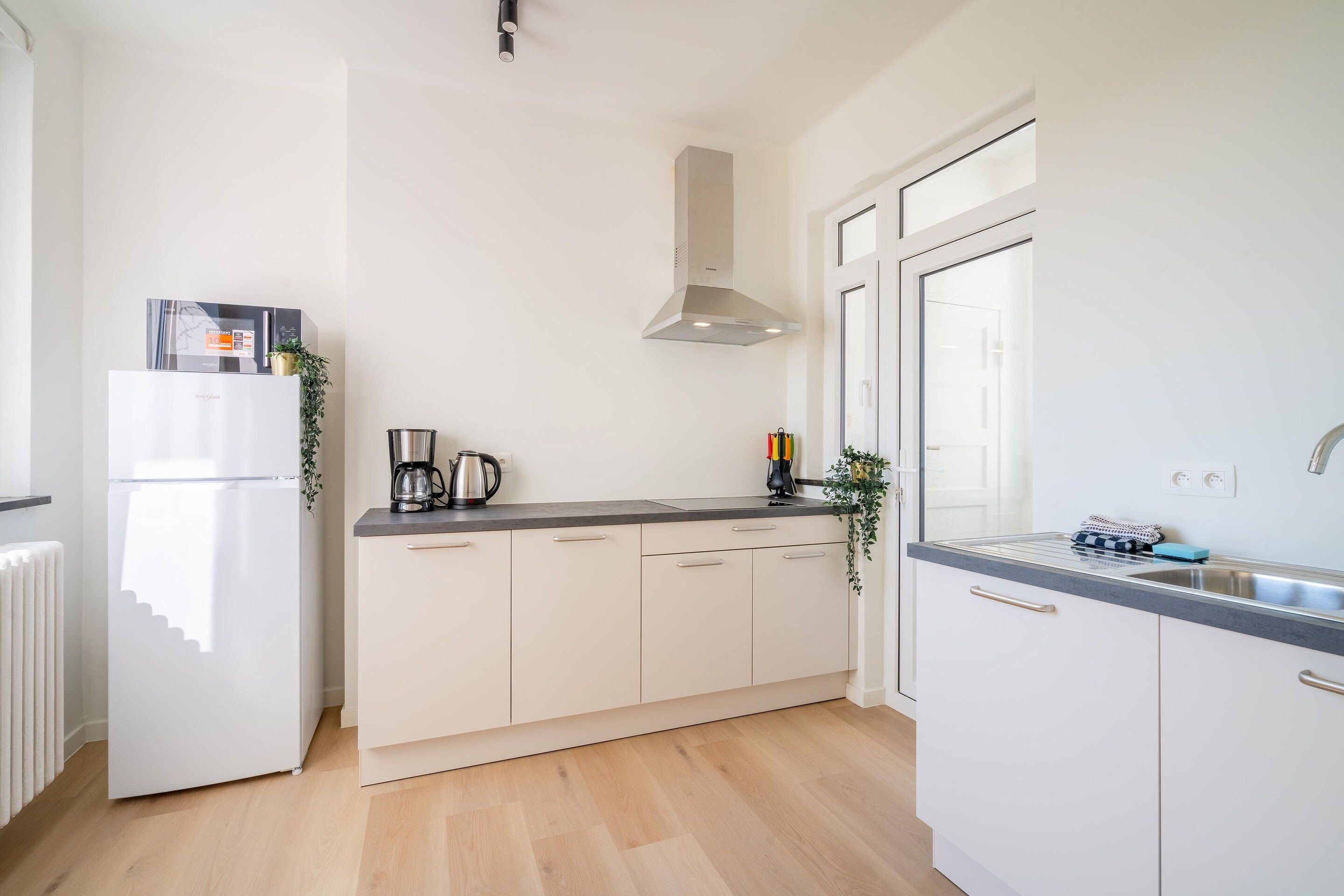 Una cocina moderna con armarios blancos, un lavamanos de acero inoxidable y un horno empotrado.