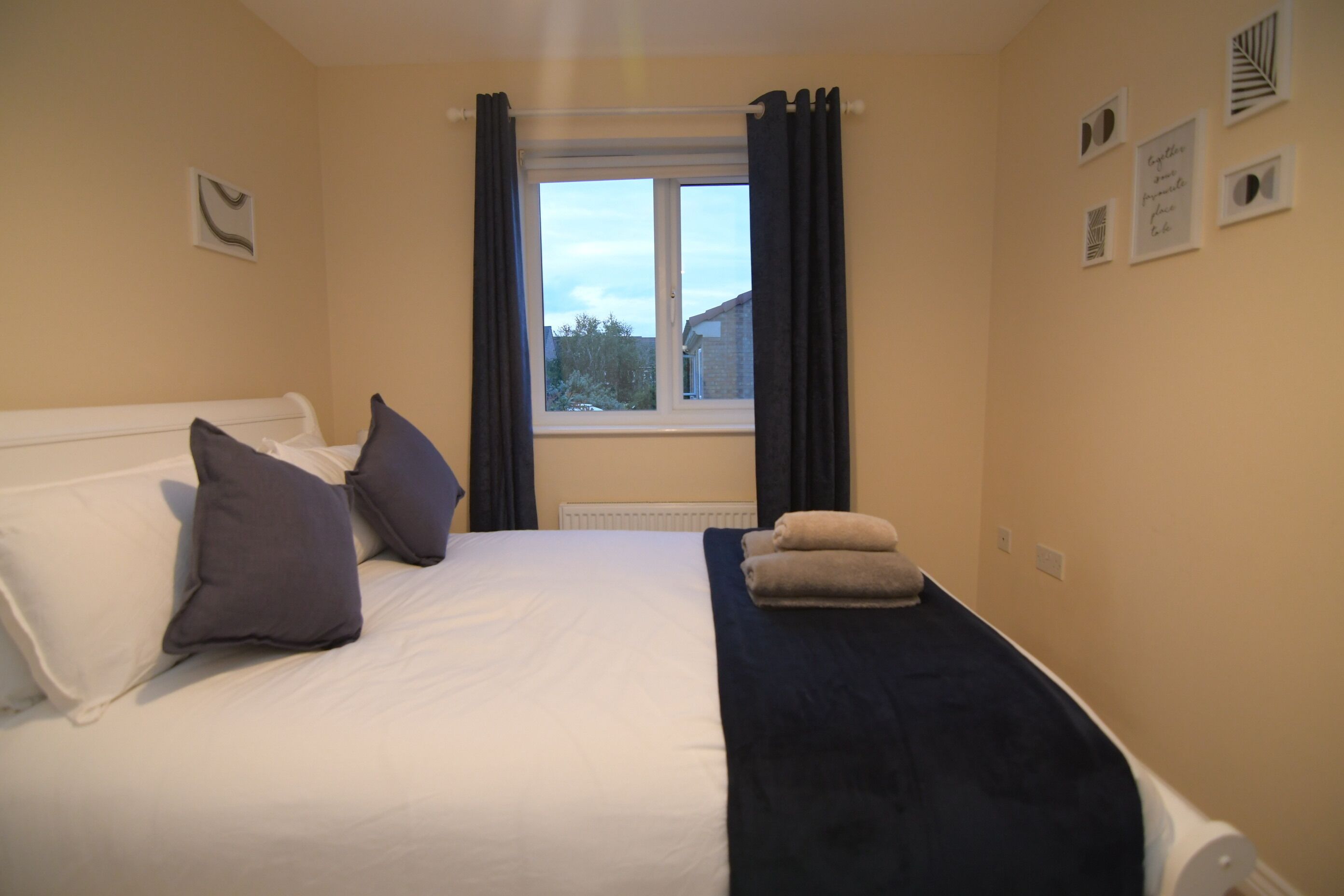 A hotel room with a bed, pillows, a window with curtains, and a radiator.