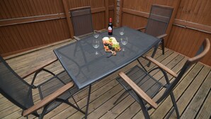 Una mesa rectangular al aire libre con cubierta de malla, rodeada por cuatro sillas con respaldos de malla. Hay una botella de vino y vasos sobre la mesa.