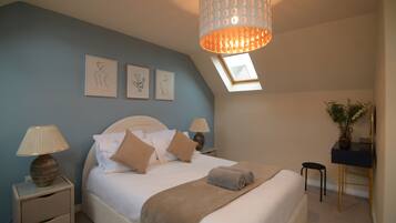 A bedroom with a bed, bedside lamps, a desk, and a skylight.
