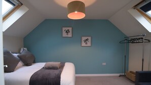 Un dormitorio con una cama, dos cuadros en la pared, una lámpara colgante y una lámpara de pie.