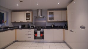 Una cocina moderna con armarios blancos, extractor de acero inoxidable y suelo de baldosas.