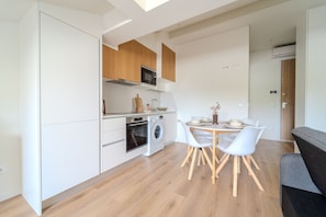 A modern kitchen with white cabinets, a built-in oven, microwave, and washing machine. There's a dining area with a round table and white chairs. - Boavista Studio by House and People (Braga)