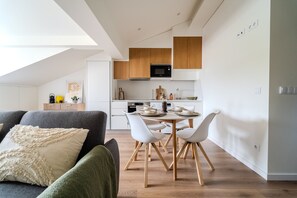 A modern kitchen with wooden cabinets, a dining table with white chairs, and a kitchenette area. - Boavista Studio by House and People (Braga)
