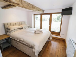 A bedroom with a bed, a nightstand, a TV, and a window with blinds. - Netherend Barn (Malvern)