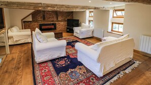 A loft-style living room with exposed wooden beams, a brick fireplace, white sofas, and a large patterned rug. - Netherend Barn (Malvern)