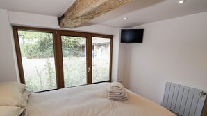 A bedroom with a large bed, a TV mounted on the wall, and a radiator. - Netherend Barn (Malvern)