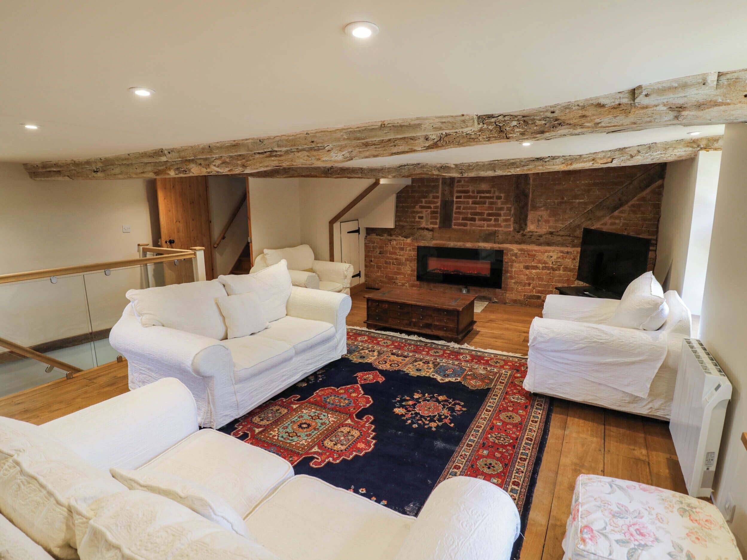 Una sala de estar con sofás blancos, un tapete estampado, una chimenea y un televisor.