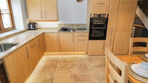 A kitchen with granite countertops, wooden cabinets, a built-in oven, and a dining area with a table and chairs. - Netherend Barn (Malvern)