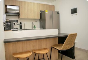 A modern kitchen with a built-in island, stainless steel appliances, and a seating area with two stools and a chair. - Luxury Apt w/Balcony-Stunning View near el Tesoro (Medellín)