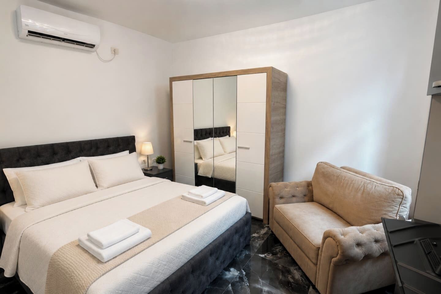 A hotel room with a bed, a sofa, a wardrobe, and a desk with a computer.