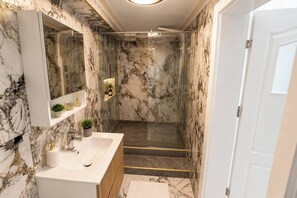 Ein Badezimmer mit Marmorwänden, einem weißen Waschbecken, einem Spiegel und einer Duschkabine.