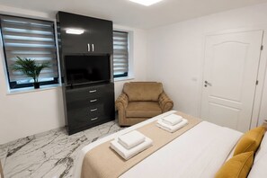 A bedroom with a bed, a chair, a wardrobe, and a television. - The Golden Suite | Premium Stay (București)