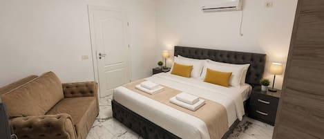 Une chambre d’hôtel avec un lit, un canapé, une table de chevet avec une lampe et un appareil de climatisation fixé au mur.