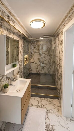 A bathroom with a marble floor, a sink, a mirror, and a shower area. - The Golden Suite | Premium Stay (București)