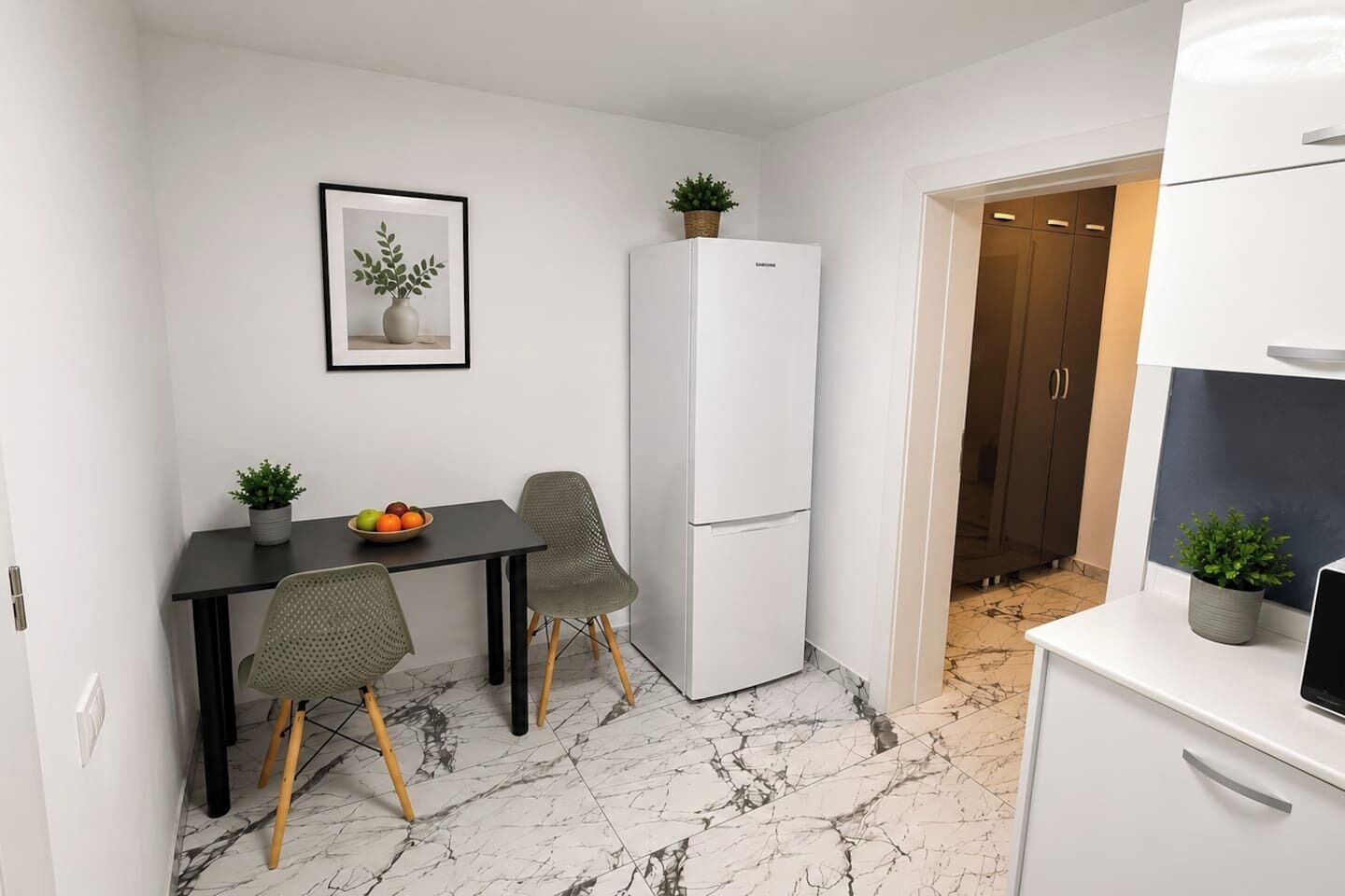 Une cuisine compacte avec un réfrigérateur blanc, une table à manger avec deux chaises et une petite plante en pot posée sur la table.