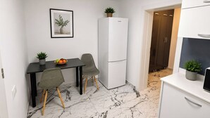 Een compacte keuken met een witte koelkast, een eettafel met twee stoelen, en een kleine potplant op de tafel.