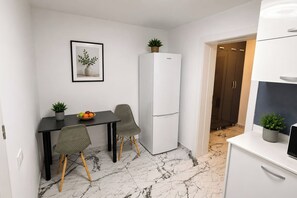 A compact kitchen with a white refrigerator, a dining table with two chairs, and a small potted plant on the table. - The Golden Suite | Premium Stay (București)