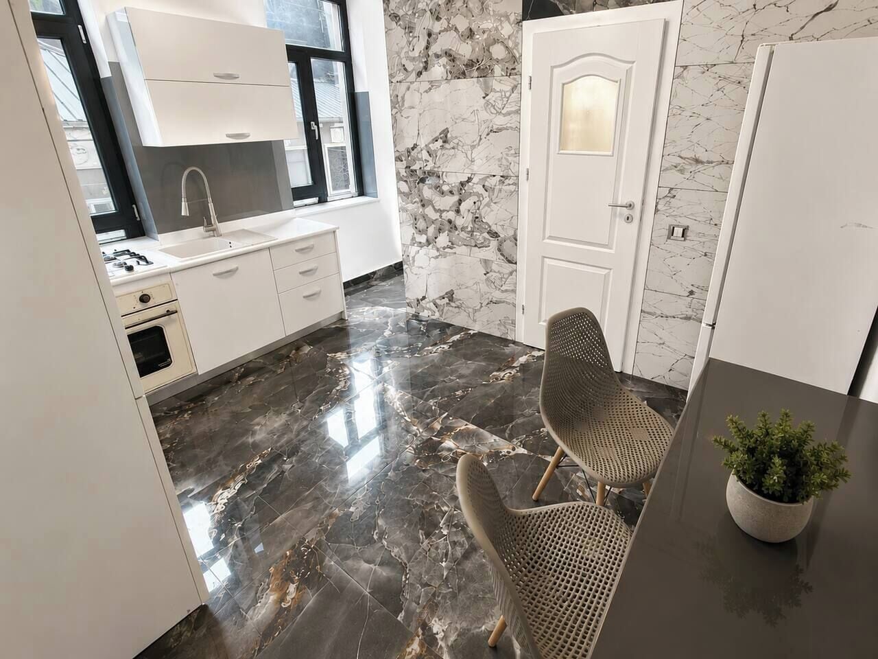 A modern kitchen with a marble backsplash, a built-in oven, and a dining area with a table and chairs.