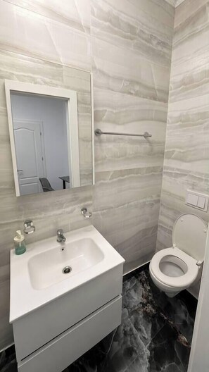 Et badeværelse med en hvid vask, spejl og toilet.