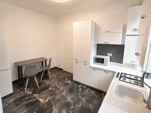 A compact kitchen with white cabinets, a gas stove, a microwave, and a small dining table with chairs. - Elegant Marble Retreat | Central Bucharest (Bucharest)