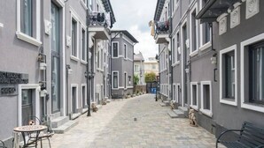 Een smalle straat met grijze gebouwen, terrasjes en een bankje.