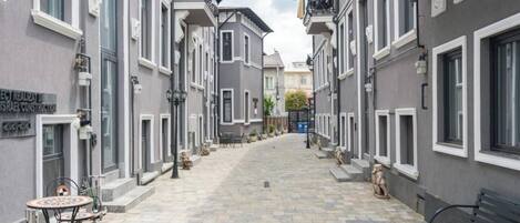 A narrow street with grey buildings, outdoor seating, and a bench.