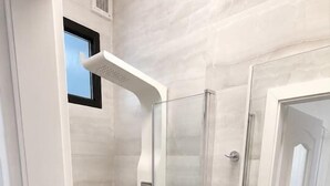 Een moderne badkamer met een douche met glazen wand, een witte wastafel en een grote spiegel.