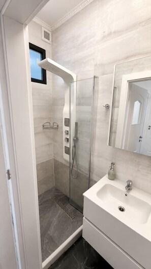 A modern bathroom with a glass-enclosed shower, a white sink, and a large mirror. - Elegant Marble Retreat | Central Bucharest (Bucharest)