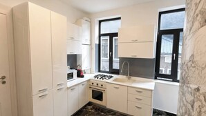 Een keuken met witte kastjes, een fornuis, een spoelbak en een raam.