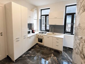 A kitchen with white cabinets, a stove, a sink, and a window. - Elegant Marble Retreat | Central Bucharest (Bucharest)