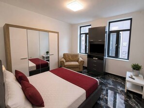 A hotel room with a bed, a chair, a wardrobe, a television, and a window. - Elegant Marble Retreat | Central Bucharest (Bucharest)