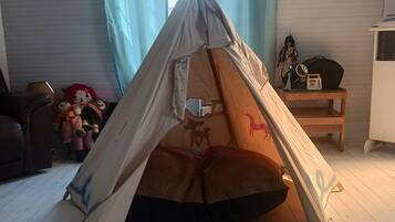 A tent set up in a room with a wooden floor, a window with curtains, and a small table with a doll and a radio.