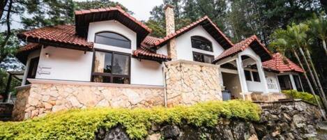 Una casa de dos pisos con base de piedra, tejado de tejas rojas y chimenea de piedra.