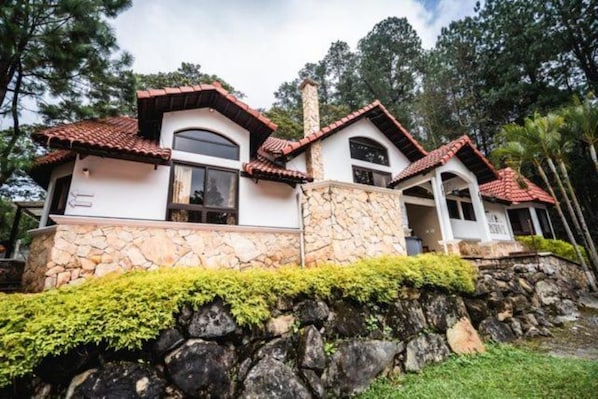 A two-story house with a stone foundation, red-tiled roof, and a stone chimney.