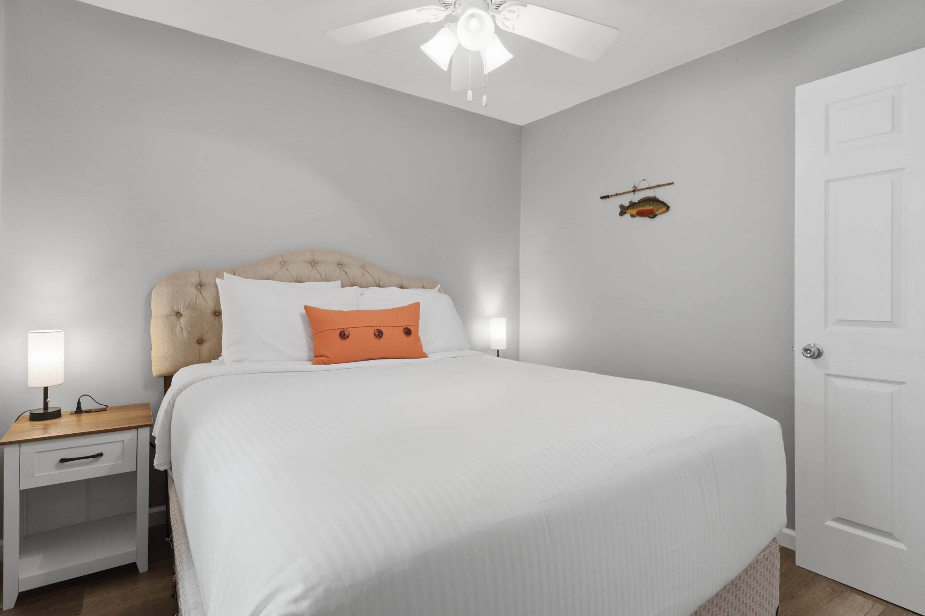 A bedroom with a bed, a nightstand, a lamp, a ceiling fan, and a door.