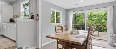 Una cocina moderna con gabinetes blancos, una mesa de comedor de madera y vistas a un balcón con follaje.