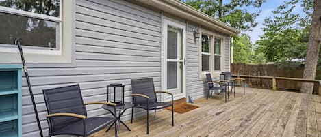 Una terraza techada con mobiliario exterior, una cerca de madera y una casa con ventanas amplias.