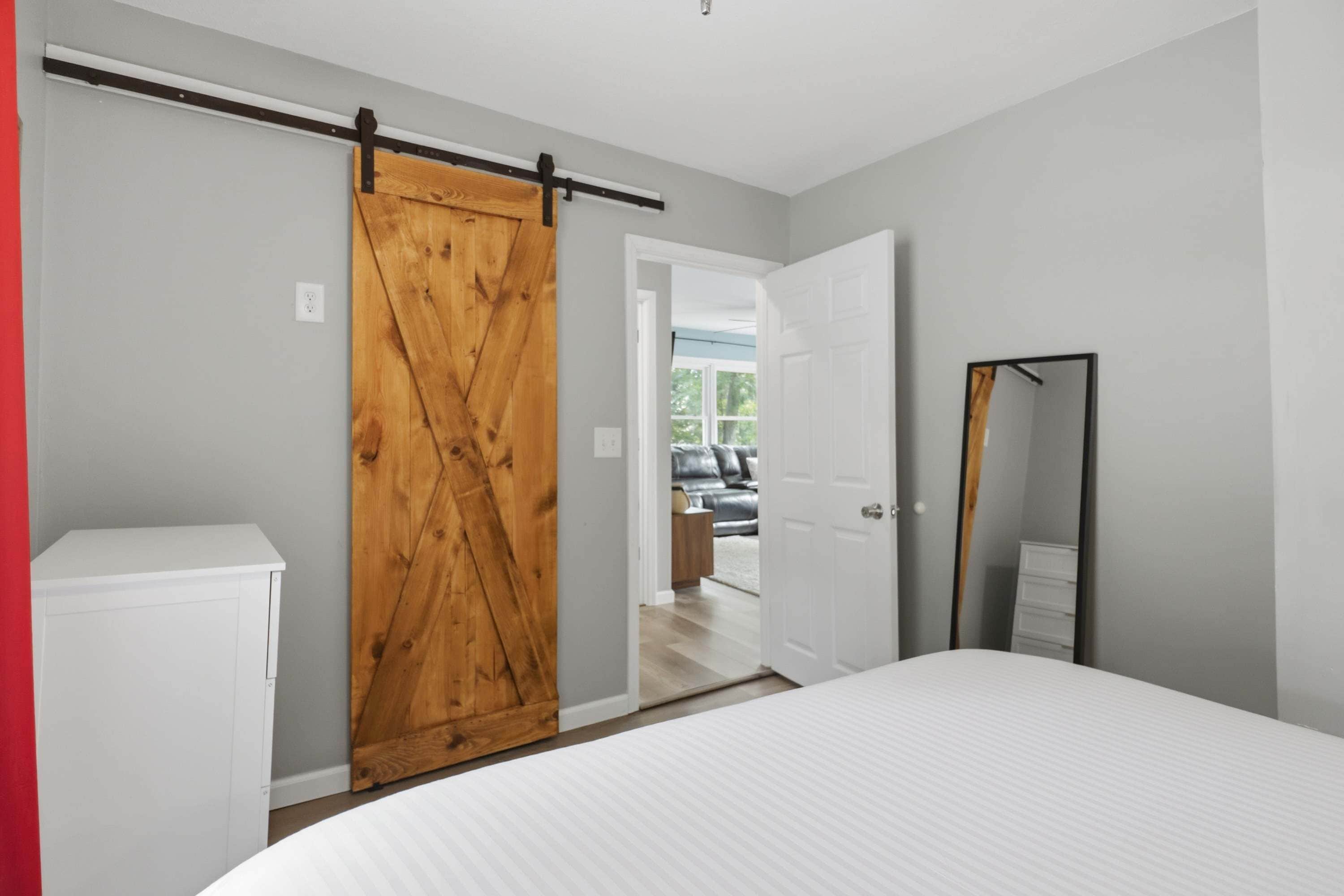 A bedroom with a bed, a wardrobe, a mirror, and a door leading to another room.