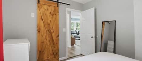 Un dormitorio con cama, armario, espejo y puerta que da a otra habitación.