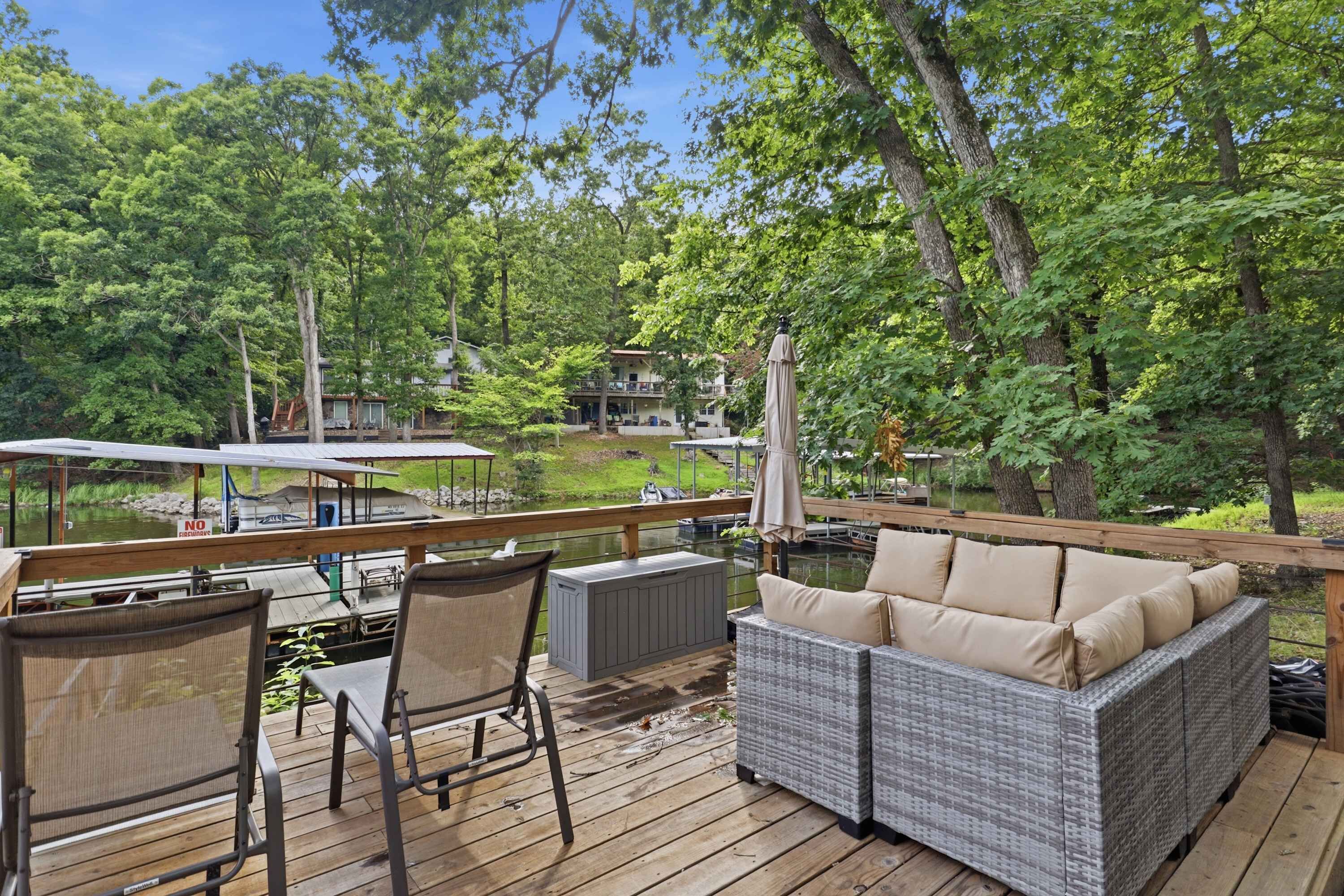 Eine Terrasse mit Gartenmöbeln, Blick auf einen See und ein Steg mit Booten.