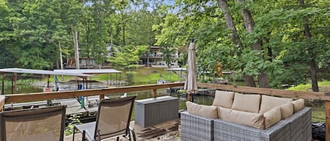 A deck with outdoor furniture, a view of a lake, and a dock with boats.