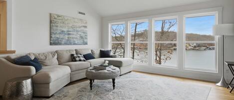 A living room with a large window, a sofa, an ottoman, and a rug.