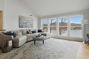A living room with a large window, a sofa, an ottoman, and a rug. - Brush Creek Retreat With Boat Slip (Sunrise Beach)