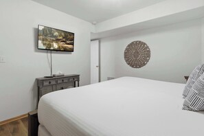 A bedroom with a bed, a flat-screen TV mounted on the wall, a bedside table with a lamp, and a decorative wall piece. - Brush Creek Retreat With Boat Slip (Sunrise Beach)