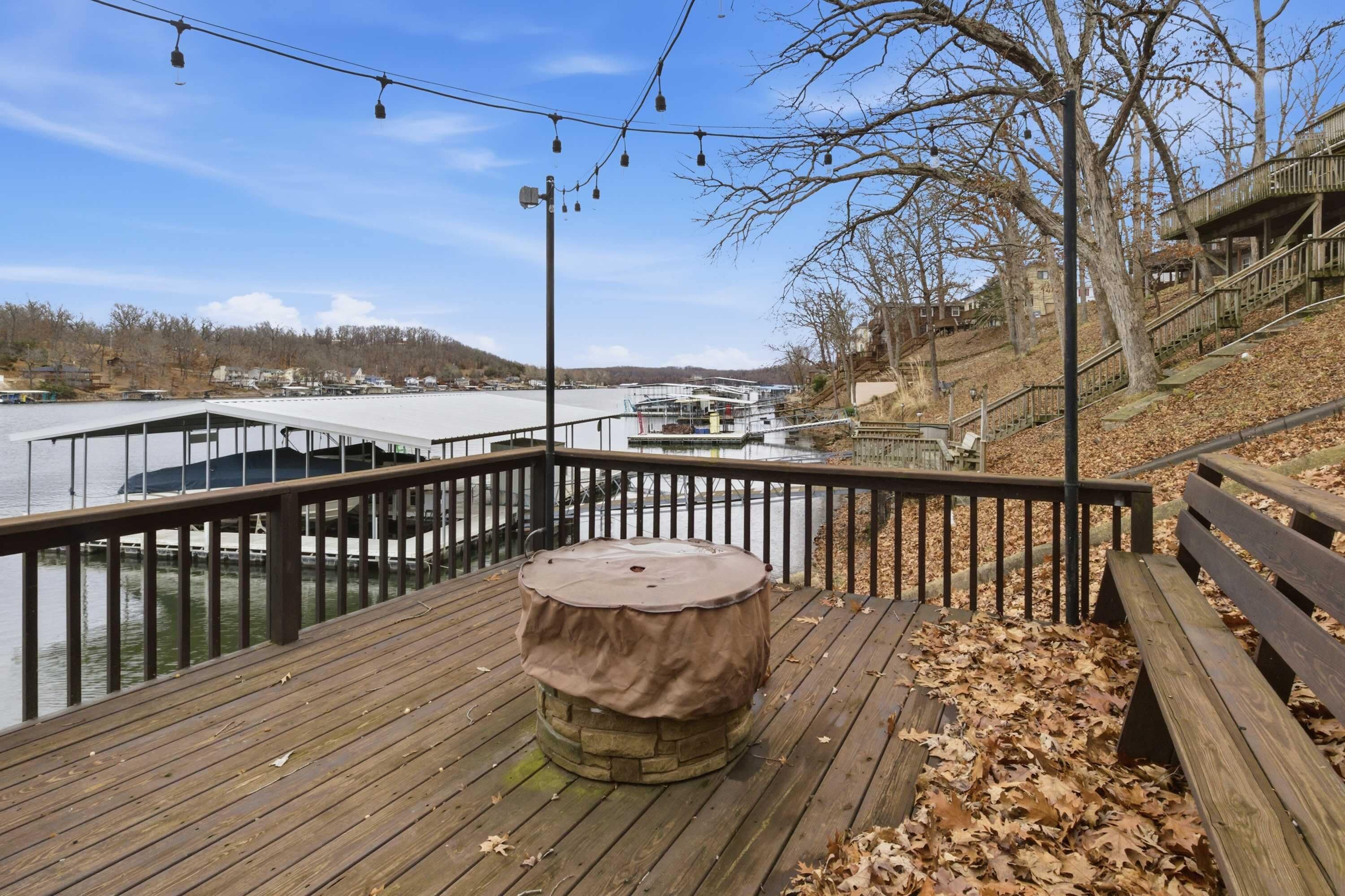 A wooden deck with a covered table, a railing, and a view of a dock with boats.