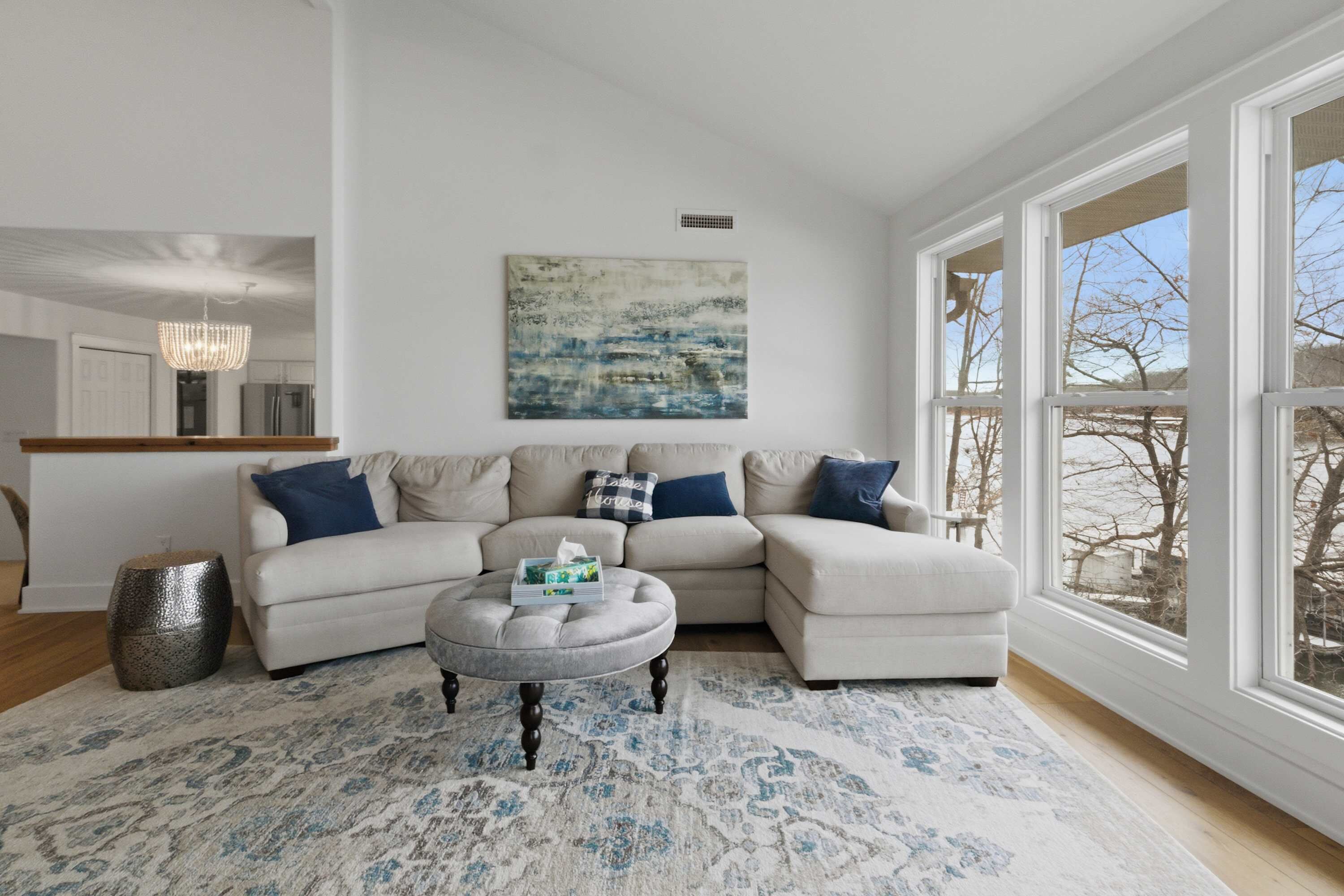 A modern living room with a sectional sofa, a round coffee table, and a large window offering a view of trees.