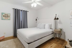 Un dormitorio con cama, ventilador de techo, mesita de noche con lámpara y un cartel que dice 'NO WAKE ZONE'.