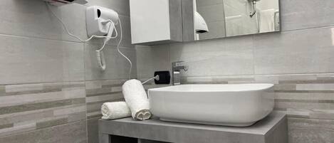 A modern bathroom with a large sink, a towel dispenser, and a mirror.