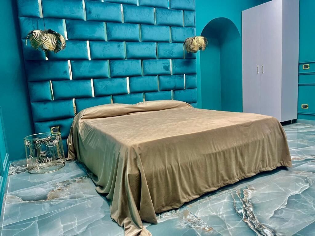 Ein Schlafzimmer mit Kopfstück aus Backsteinoptik, einem Bett mit beige farbenem Bettbezug, einem kleinen Nachttisch und einem Kleiderschrank.